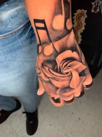 a black and grey rose tattoo on a person's hand