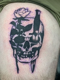 a tattoo of a skull with roses and a knife