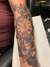 a tattoo with a clock and roses on the forearm