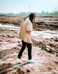 a man with dreadlocks walking through a muddy area